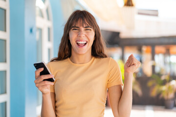 Young woman at outdoors using mobile phone and doing victory gesture