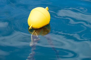 Gelbe Boje mit Vertäuung auf ruhigem blauen Wasser in einem Hafen (nautic sea buoy)