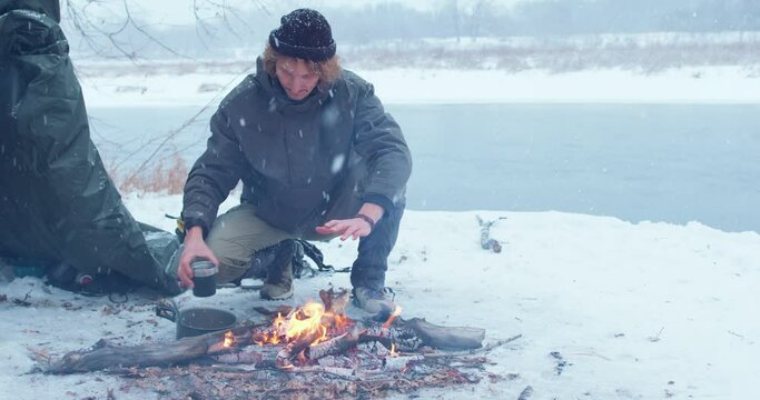 Slow motion, hicker rubbing hands, palms, eating food, drinking coffee from thermo mug Extreme holiday Traveler has dinner sits behind campfire outdoors