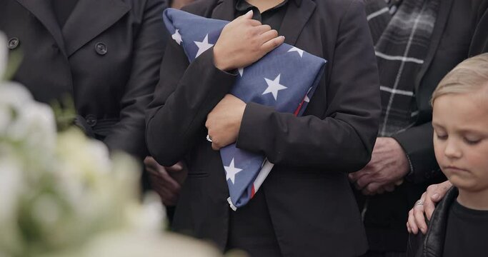 Funeral, cemetery and woman with American flag for veteran for respect, ceremony and memorial service. Family, depression and sad people by coffin in graveyard for military, army and soldier mourning