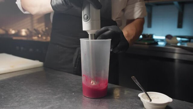 Pastry chef prepares pink raspberry fruit sauce for cheesecake