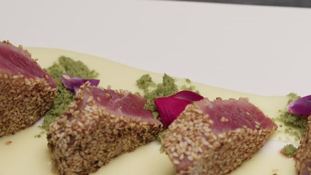 Cook is serving crusted tuna fillets with sesame seeds on a sauce