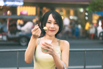 Young adult asian foodie woman eating thai dessert at china town street food