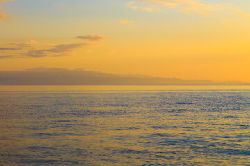 Fototapeta premium Clear water texture in blue and orange. sky and clouds reflection. Background of the ocean and the sea backlit by the sun.