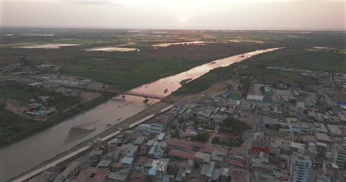 Aerial shot of Tumbes river, bridge and city at sunset. Tropical city at north of Per&uacute;. 