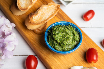 Traditional Italian pesto sauce served with mozzarella cheese, tomatoes and bruschetta on a white wooden table