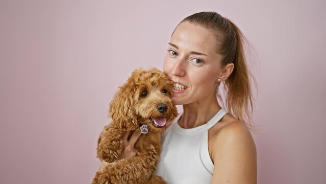 Young caucasian woman with dog smiling kissing over isolated pink background