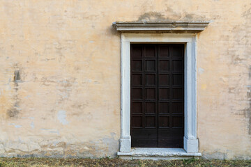 Fototapeta na wymiar Vecchia porta di legno sulla parete gialla con erba in primo piano.