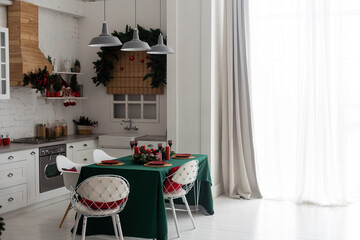 kitchen decorated with pine garlands and Christmas toys. the table and near is worth Christmas tree. interior bright kitchen decorated for Christmas.