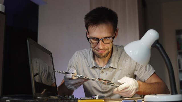 Repairman looks at motherboard of broken laptop, takes his head and gets upset. Complex malfunction of semiconductor components of electronic equipment in workshop for repair and maintenance.