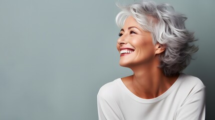 Beautiful gorgeous 50s mid age beautiful elderly senior model woman with grey hair laughing and smiling. Mature old lady close up portrait.