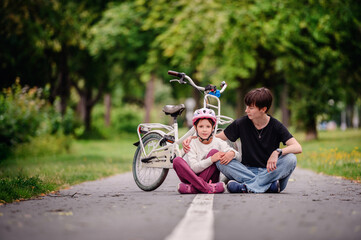 Obraz premium Young mother in jeans and black t-shirt teaching and sitting with her daughter on track in summer parks while speaking