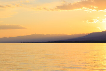 Obraz premium Beautiful cloudy sunset over the sea and mountains. Bright sky in the rays of the orange sun. natural texture