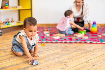 Toddler girl playing with toy car in kindergarten on a wooden floor