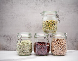 Green beans, kidney beans, split peas, rice, chickpeas. Glass jars on white marble table and...