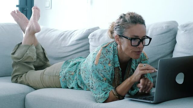 Smart working and surfing the net. One woman at home laying on sofa having relax and indoor technology leisure activity with wireless connection. Modern people lifestyle using laptop on the couch