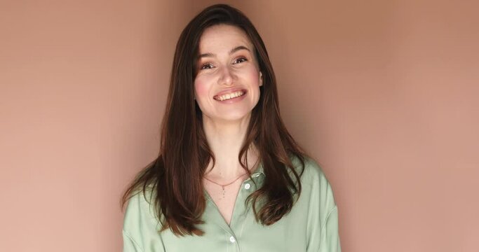 Happy friendly young woman waves palm in hello gesture welcomes someone with hospitable expression expresses positive emotions dressed green shirt isolated over beige background. Hi to all of you.