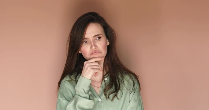 Pensive puzzled young girl thinking isolated on beige background. Looking aside up put hand prop up on chin, finger on lips. Thoughtful woman thinks deeply chooses or ponders plan, not sure, not know.