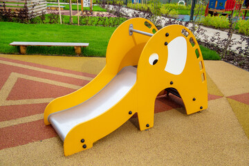 A yellow wooden slide in the form of an elephant on the playground in kindergarten on a clear sunny day. Playgrounds, toys, sports.