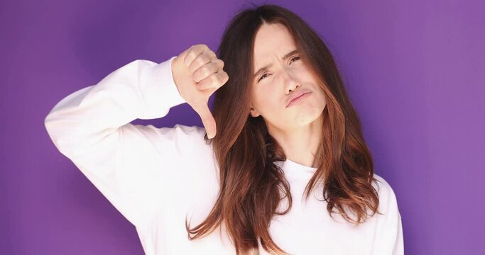 Young woman in white long sleeve making good-bad sign isolated on purple background. Girl make choice, or makes a decision thumb up or thumb down, like or dislike, yes or no. Girl shrugs, not sure.