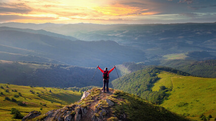 Hiker girl with raised arms meets sunset on the mountain peak
