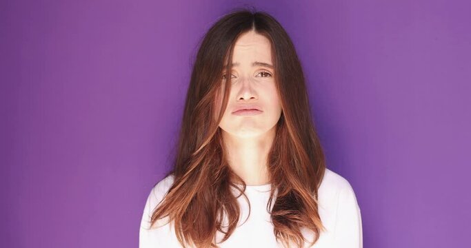 Angry sad brunette young woman in white long sleeves posing isolated on purple background studio. Woman shout screaming news with hand near mouth shocked wow.