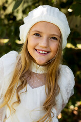 a beautiful happy blonde girl in a white blouse and a hat with a pompom is standing on the street