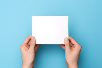 A human hand holding a blank sheet of white paper or card isolated on blue background