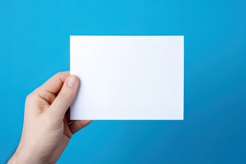 Obraz premium A human hand holding a blank sheet of white paper or card isolated on blue background
