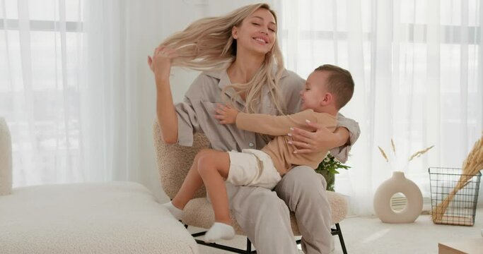 Mother having fun and tickling her little cute son on sofa at home. Slow motion Love relationship, mommy and kid enjoy funny activities on weekend at home, playing together, careless happy childhood