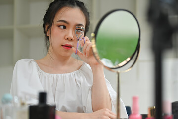 Beautiful young woman using eyelash curler curling eyelashes before mascara in front of mirror