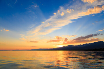 Colorful sunset on the sea. Mountain lake in the rays of the orange sun. Kyrgyzstan, Lake Issyk-Kul.