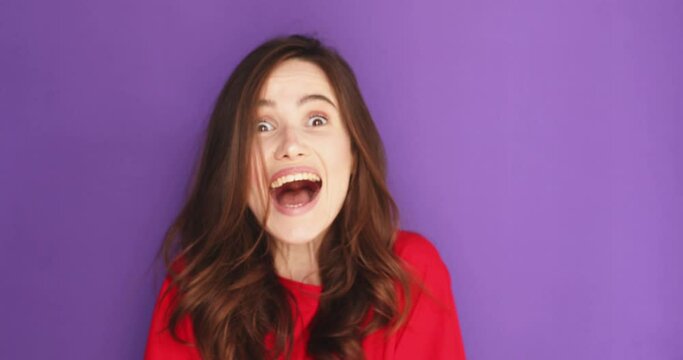 Doubtful brunette woman look skeptical with distrust at camera and next say wow, she is happy, winner. Girl happy screaming and joyful isolated on purple background.