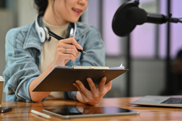 Smiling woman radio host in headphone talking through microphone for recording conversation for...