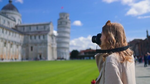 Young blonde female tourist taking photos of the famous Leaning Tower of Pisa. Vacation in Italy, traveling off season. High quality FullHD footage