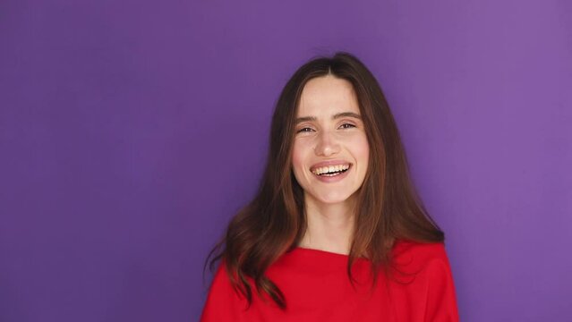 Young brunette woman blowing kisses against purple wall background. Female person wish good luck. Female person with tenderness emotion. Close up portrait of happy girl send air kiss, love concept.