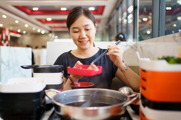 Happy - cheerful Asian fat woman enjoy eating a traditional Asian Hotpot or Sukiyaki in the Asian Hotpot restaurant.
