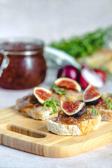 Homemade caramelized onion confit or marmalade on a slices of baguette with liver pate, figs and fresh thyme served on a wood serving board, selective focus. Healthy organic food.