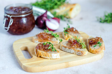 Homemade caramelized onion confit on a slices of bread with liver pate, fresh thyme, served on a wood serving board, selective focus. Healthy organic food