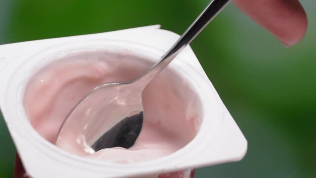 macro videography, Slow motion yogurt with spoon in cup. Hand woman takes fruit yogurt in cup in package with spoon.Eating healthy food in form of fermented milk product.
