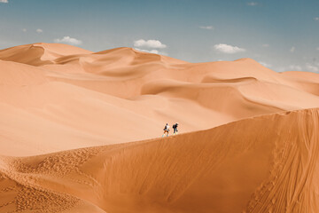 Two people hiking up a sand dune at Kumtag Desert, Xinjiang