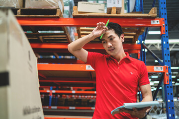 A stressed male manager or worker sits leaning against a box holding a tablet and in a warehouse....