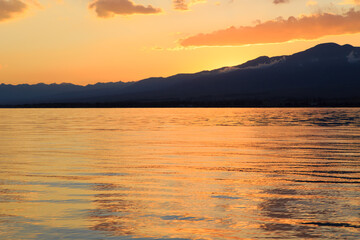 Fototapeta premium Colorful sunset on the sea. Mountain lake in the rays of the orange sun. Kyrgyzstan, Lake Issyk-Kul.