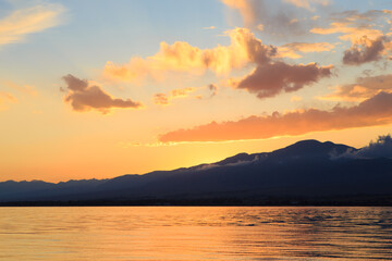 Beautiful cloudy sunset over the sea and mountains. Bright sky in the rays of the orange sun. natural texture