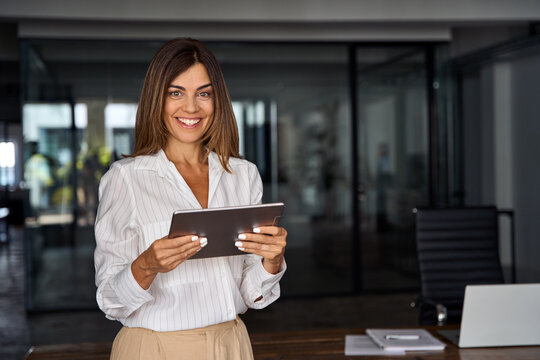 Latin Hispanic 40s Years Mature Business Woman Looking At Camera. Smiling European Businesswoman CEO Holding Digital Tablet Using Fintech Tab Online Application Standing In Modern Office, Copy Space