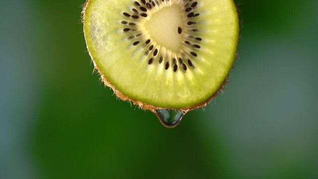 Creative mockup of sliced kiwi slice and water. Splashes on green background. Freshly chopped kiwi splashes in cold water in isolation. Concept of healthy eating and freshness. Slow motion