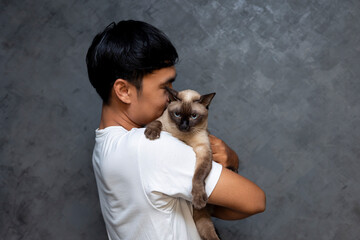 Asian man holding siamese cat with black background. Asian man hugging a cat to show love for pets.