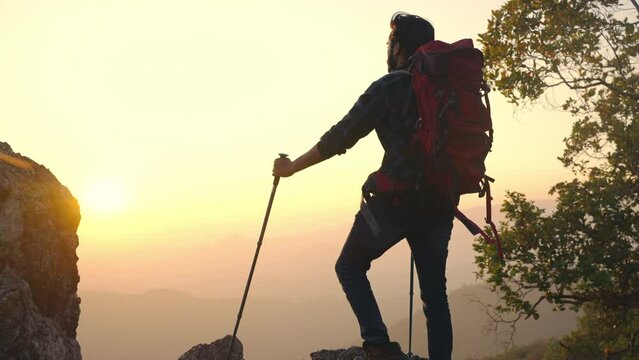 Portrait of Indian man traveler standing on mountain peak and looking beautiful nature at sunset. Handsome guy enjoy adventure outdoor lifestyle travel nature and hiking on summer holiday vacation.