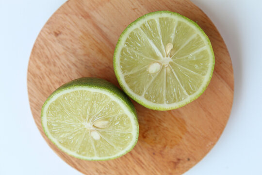 Halves of Green Lime, on wooden base, isolated on white background