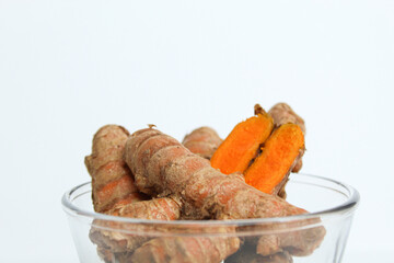Turmeric or Curcuma longa rhizome in transparent bowl, isolated in white background. Side view
